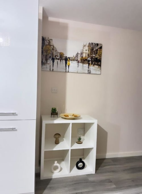 White shelving unit with decorative items and framed rainy street scene in modern Manchester hotel room