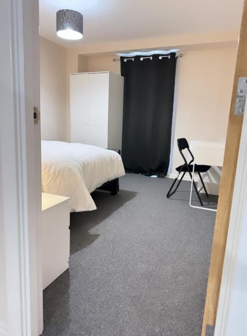 Modern bedroom at Cila Property Manchester with white bed, black curtain, gray carpet, and minimalist decor