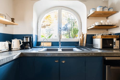 Cuisine contemporaine bleue avec double évier, étagères bois et fenêtre en arche au gîte Le Mas F à Saint-Rémy-de-Provence