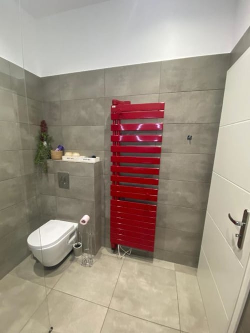 Salle de bain moderne avec sèche-serviettes chauffant rouge, toilettes murales, carrelage gris et éclairage plafond lumineux