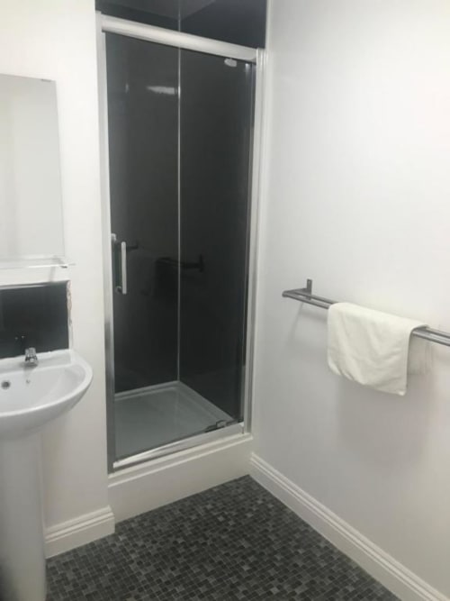 Modern bathroom with black tiled shower enclosure, white sink, towel rack, and dark floor in Ball Alley Family Room, Stanley
