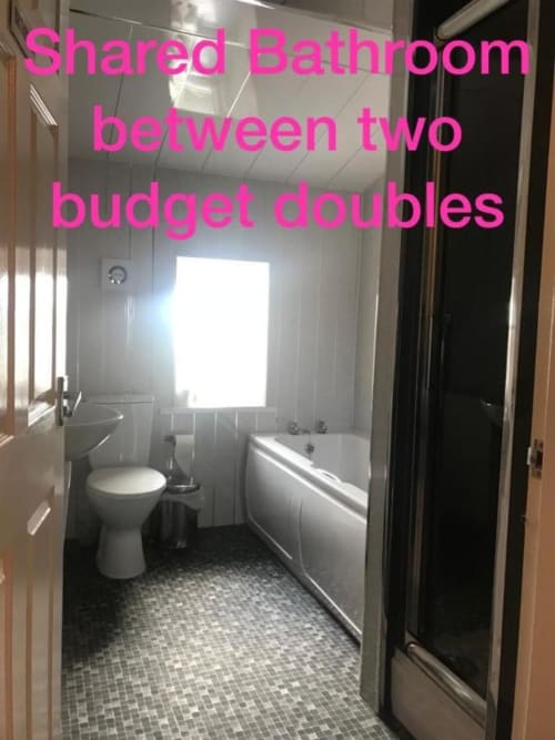 Shared bathroom between two budget doubles at The Ball Alley, Stanley. Features toilet, bathtub, sink and tiled flooring.