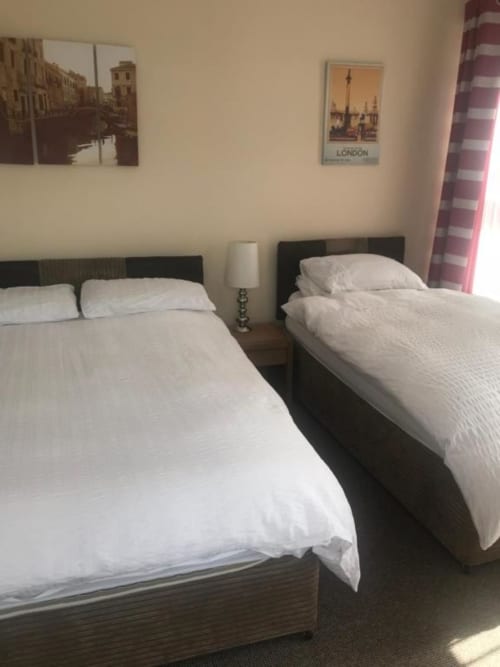 Family room at The Ball Alley B&B in Stanley showing two single beds with white linens, dark headboards, and striped curtains
