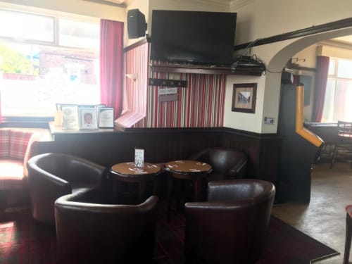 The Ball Alley B&B lounge in Stanley, County Durham features black leather seating, wooden side tables, and wall-mounted TV