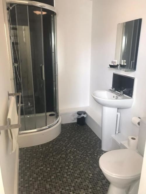 Modern bathroom at The Ball Alley B&B Stanley, featuring shower enclosure, pedestal sink, and toilet with dark tile flooring