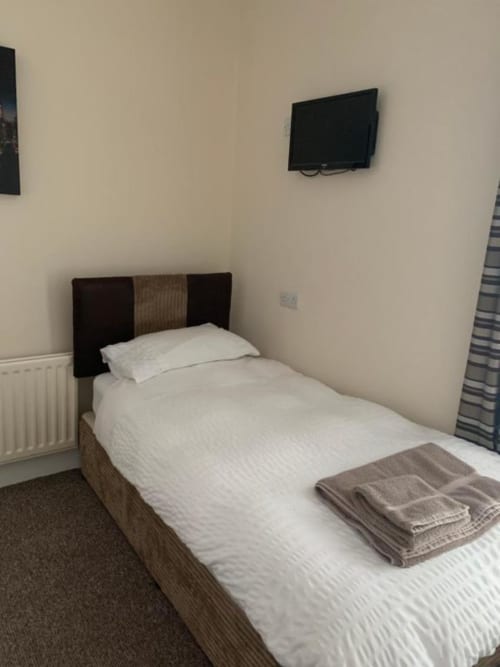 Single bedroom at The Ball Alley B&B in Stanley with white bedding, dark headboard, wall-mounted TV, and radiator heating