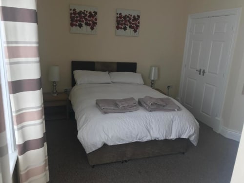 Modern double bedroom at The Ball Alley B&B in Stanley, County Durham, with black bed frame, white bedding, striped curtains,