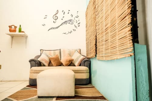 Acogedora sala de estar del apartamento LLUNA en Oaxaca con sofá beige, cojines decorativos, detalles tejidos y arte mural de notas musicales