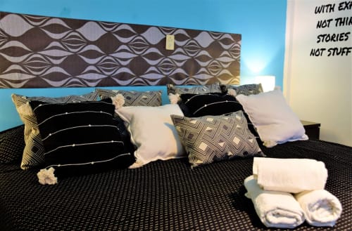 Cama del departamento LLUNA en Oaxaca con cabecera geométrica negra, almohadas estampadas y toallas enrolladas sobre edredón oscuro