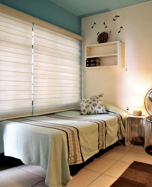 Acogedora habitación del apartamento LLUNA en Oaxaca con techo turquesa, persianas blancas, estantes de madera y ropa de cama estampada.