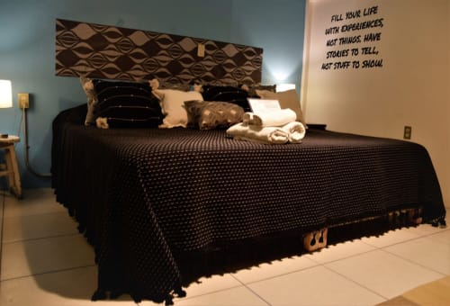 Dormitorio moderno en apartamento LLUNA Oaxaca con cama negra, cabecera estampada y frase inspiradora en la pared