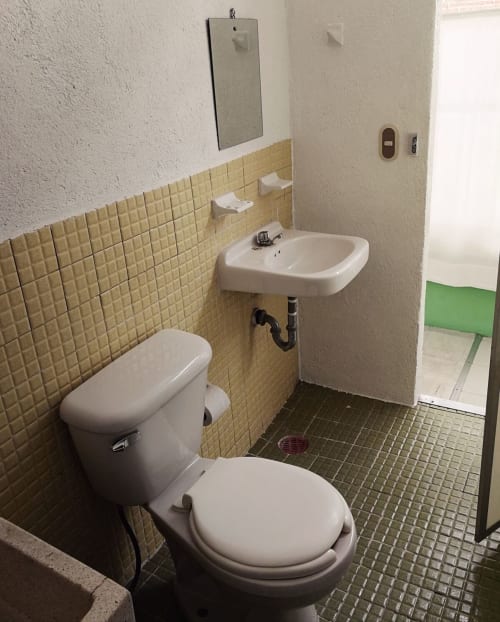 Pequeño baño del apartamento LLUNA en Oaxaca con inodoro, lavabo, azulejos amarillos y piso oscuro
