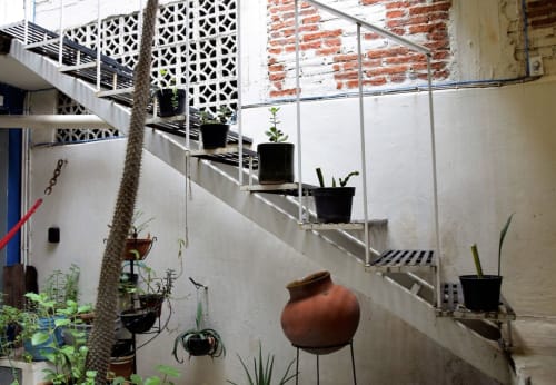 Patio de apartamento en Oaxaca con escalera de caracol, plantas en macetas y olla de barro tradicional en hotel LLUNA
