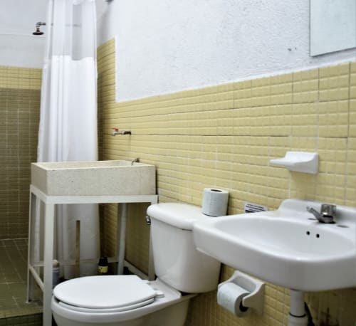 Baño del departamento LLUNA en Oaxaca con azulejos amarillos, lavamanos blanco, inodoro y cortina de ducha