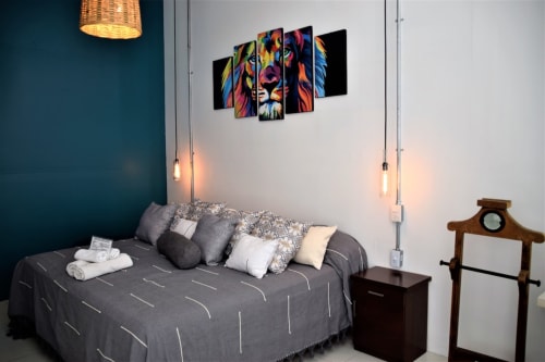 Dormitorio moderno en apartamento LLUNA de Oaxaca con arte de león colorido, cama gris, luces colgantes y pared acentuada en azul verdoso
