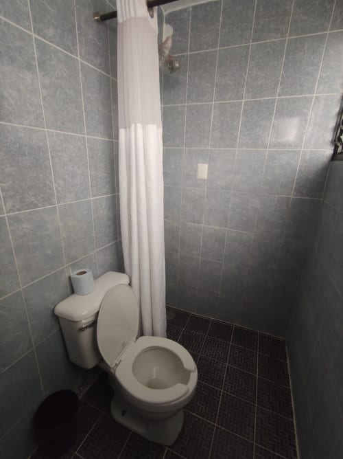 Baño del departamento LLUNA en Oaxaca con inodoro, cortina de baño y paredes de azulejos grises