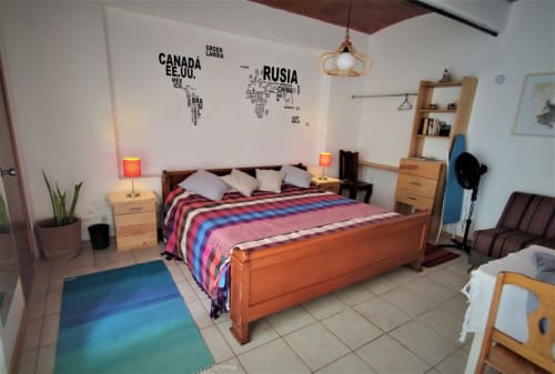 Dormitorio colorido en apartamento LLUNA de Oaxaca con cama de madera, mapa mundi en la pared y alfombra azul turquesa