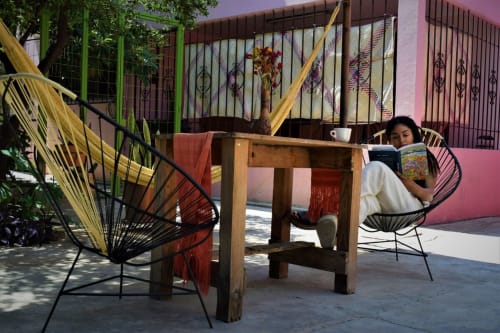 Huésped relajándose en silla colorida en el patio de LLUNA Oaxaca con textiles tradicionales y mesa de madera