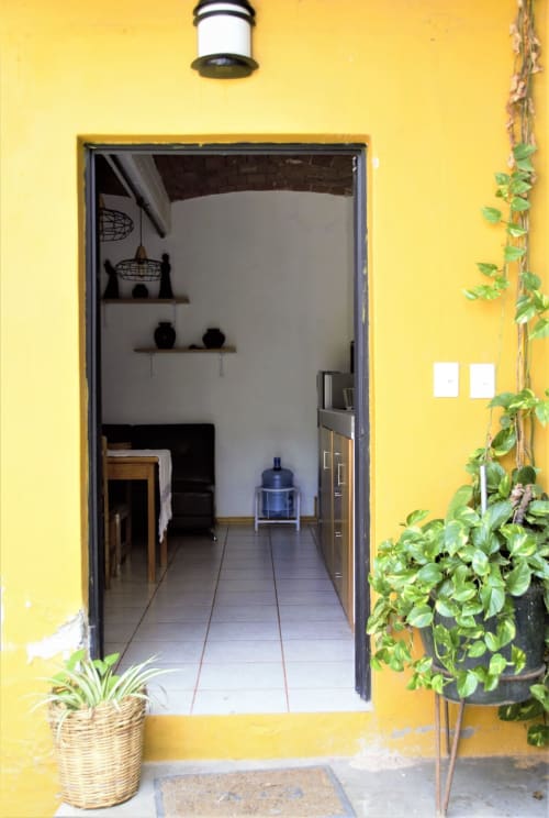 Entrada amarillo brillante del departamento LLUNA en Oaxaca con puerta abierta, plantas en macetas e interior minimalista visible