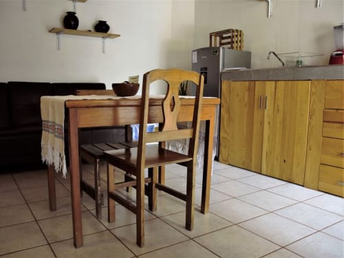 Comedor de madera cálida y sillas en cocina de apartamento oaxaqueño luminoso con pisos de azulejo y alacenas de almacenamiento