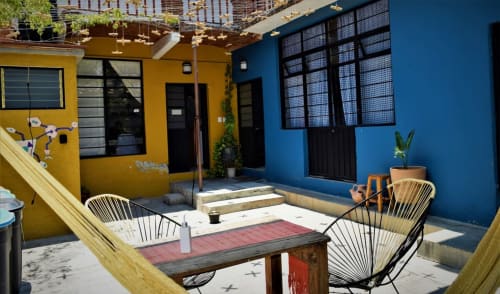 Patio del apartamento LLUNA en Oaxaca con edificios amarillos y azules, sillas modernas, mesa de comedor y plantas en macetas