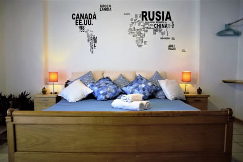 Recámara del departamento LLUNA en Oaxaca con cama de madera, almohadas azules, vinilo de mapa mundial e iluminación ambiental