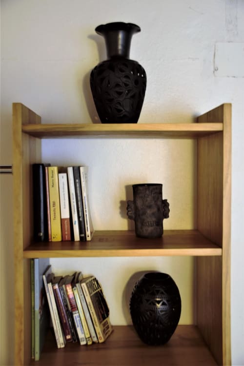 Estantería de madera en departamento LLUNA Oaxaca con vasijas decorativas negras talladas y libros apilados