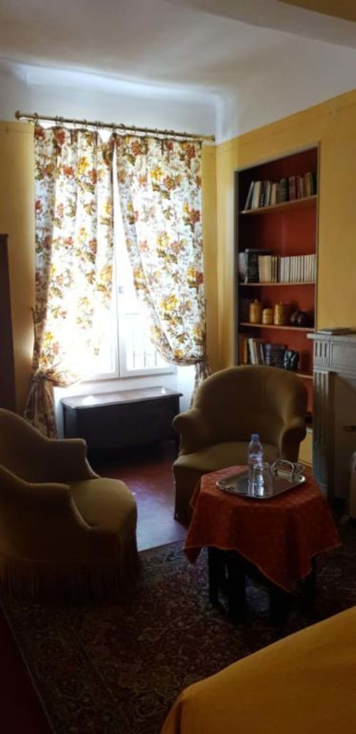 Chambre douillette à La Cordeline B&B à Brignoles avec rideaux fleuris, fauteuils, bibliothèque et vue sur la ville