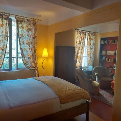 Chambre jaune éclatant à La Cordeline B&B à Brignoles avec rideaux à motifs floraux, vue sur la ville et coin lecture