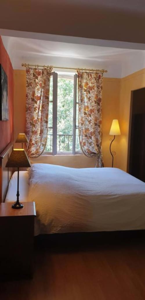 Chambre lumineuse à La Cordeline B&B à Brignoles avec murs jaunes, rideaux fleuris et vue sur la ville
