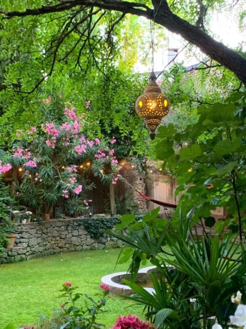 Cour enchantée du B&B La Cordeline à Brignoles avec lanterne en laiton suspendue, fleurs roses et feuillage verdoyant