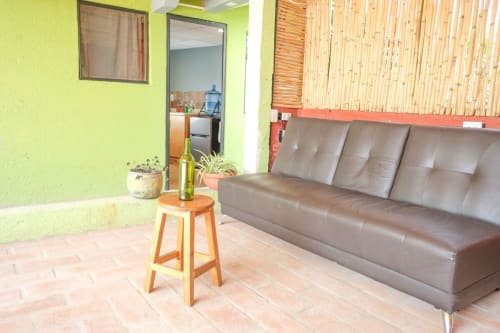 Sala de estar en tonos verde brillante del departamento LLUNA en Oaxaca con sofá de cuero gris, banqueta de madera y piso de barro
