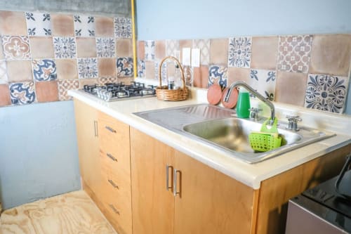 Cocina del departamento LLUNA en Oaxaca con azulejos decorados, muebles de madera y lavaplatos de acero inoxidable.