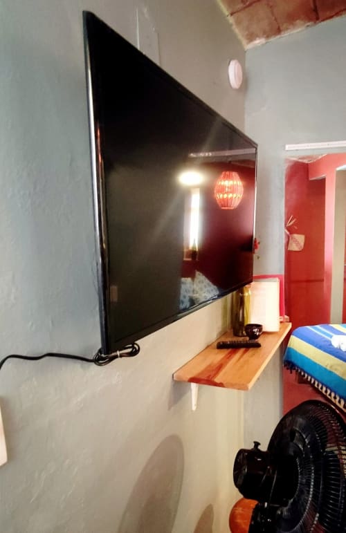 Televisor montado en pared en apartamento LLUNA, Oaxaca, con repisa de madera y acentos de diseño rojo