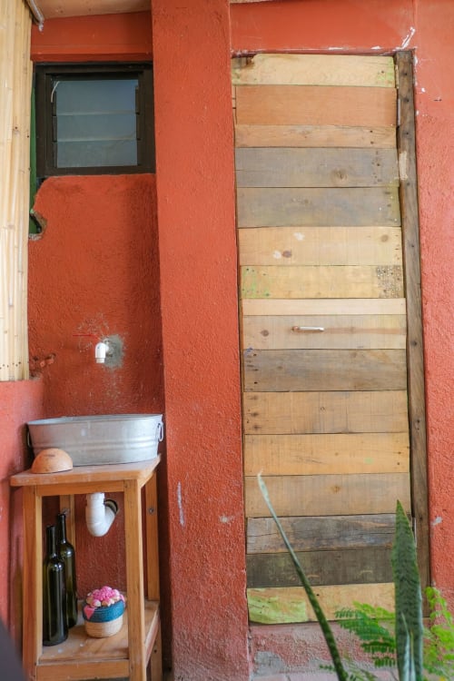 Entrada del apartamento LLUNA en Oaxaca con paredes rojas, puerta de madera, mesita con fuente y flores