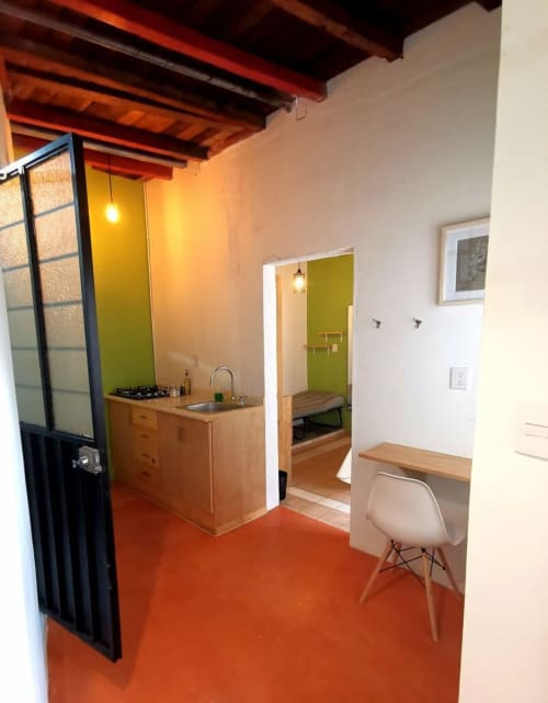 Moderno departamento LLUNA en Oaxaca con pisos pulidos naranja, cocina de madera, pared acentuada verde limón y vigas de techo expuestas