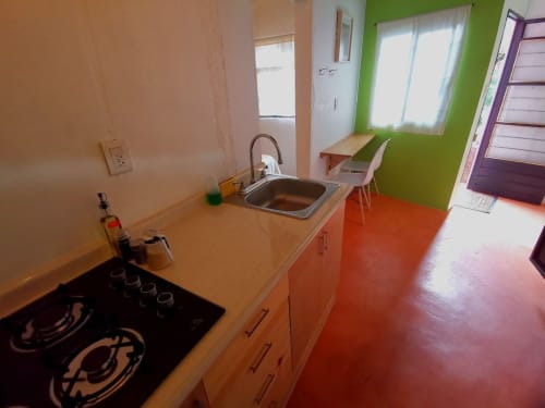 Cocina colorida del hotel LLUNA en Oaxaca con paredes verdes, piso rojo y fregadero de acero inoxidable.