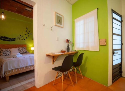 Apartamento luminoso en el hotel LLUNA de Oaxaca con paredes verde lima, zona de trabajo con sillas negras y dormitorio con madera