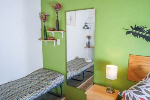 Luminosa habitación verde en apartamento LLUNA en Oaxaca con camas gemelas, espejo, plantas en macetas y lámpara de madera en la mesilla