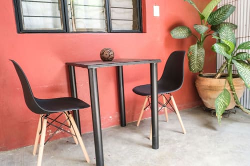 Sala de estar moderna en LLUNA Oaxaca con pared rojo coral, mesa negra, dos sillas y planta verde en maceta