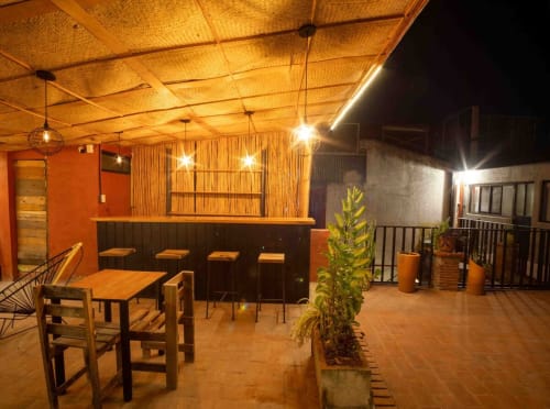 Terraza en la azotea del departamento LLUNA en Oaxaca por la noche, con bar de madera, mesa de comedor e iluminación ambiental cálida