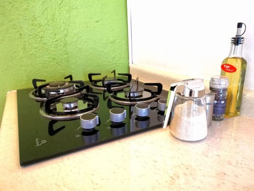 Estufa de gas negra con cuatro quemadores y perillas de control, mostrador de cocina con botella de aceite y recipientes en LLUNA Oaxaca
