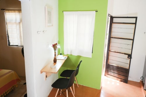 Pared de acento verde brillante con escritorio de madera, sillas negras y cortinas blancas en el departamento LLUNA, Oaxaca de Juárez México