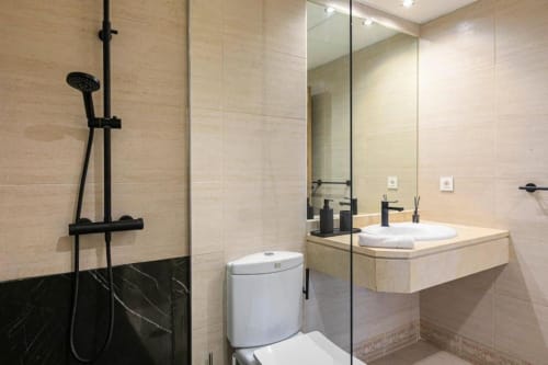 Modern bathroom in Marbella apartment with walk-in shower, floating sink vanity, and black marble accents