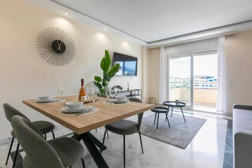 Modern dining area with wooden table, city view balcony at Marbella Home Rentals Marina Banús apartment
