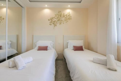 Twin bedroom in Marina Banús apartment, Marbella with two single beds, white linens, burgundy accents, and modern decor