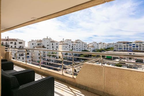 Sunny balcony view of Marbella cityscape with white Mediterranean buildings and street below at Marina Banús apartment.