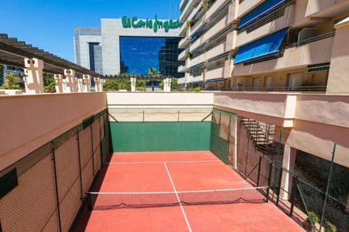 Rooftop tennis court at Marbella Home Rentals in Puerto Banús with modern apartment buildings overlooking the court