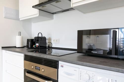 Modern kitchen in Marbella apartment with microwave, stovetop, dishwasher, and black countertop with white cabinetry