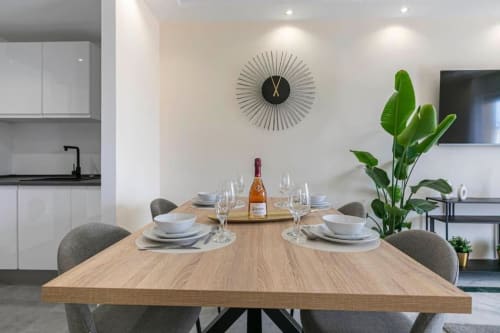 Modern dining table set for four with white place settings, wine bottle, and geometric wall clock in Marbella Home Rentals